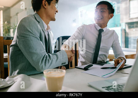 Two successful business men shaking hands with each other after a deal. Asian businesspeople sitting at coffee shop making a hand shake after a succes Stock Photo