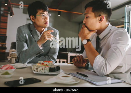 Two business professionals discussing working over a lunch at restaurant. Businessmen talking with colleague while having food at restaurant. Stock Photo