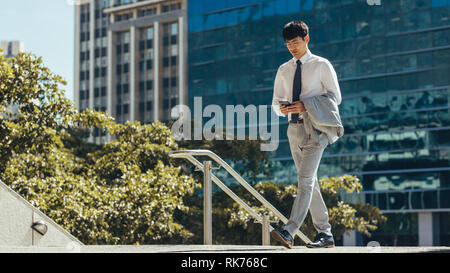 Asian businessman walking outdoors in city using smart phone. Man professional walking and using a smart phone outdoor. Stock Photo