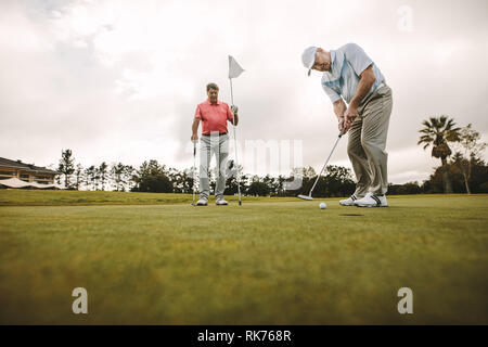 Low angle view of senior golfer on putting green about to take the shot. Male golf player putting on green with second male player in the background h Stock Photo