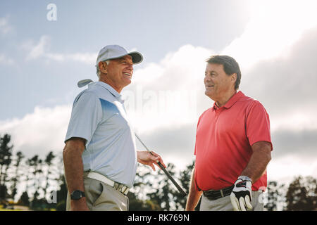 Two senior golf players with golf clubs standing together and talking between the game on a sunny day. Professional golfers having chat between the ga Stock Photo