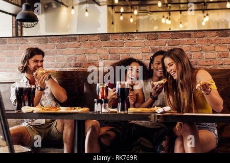 Group of friends having pizza at cafe. Cheerful young people eating pizza and enjoying at a fast food restaurant. Stock Photo