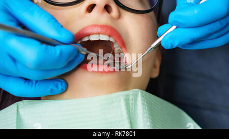 Routine examination at dentist. Young girl with open mouth. White teeth. Dentist's hands in protective gloves with medical instrument. Close-up. Stock Photo