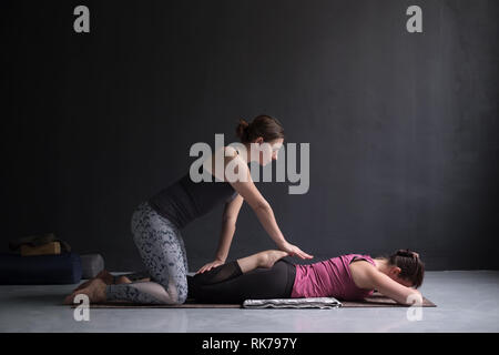 Coach helping woman practicing yoga, doing Bhekasana exercise together Stock Photo