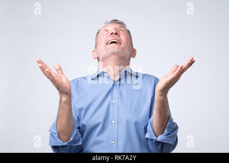 Happy senior man praying to god with his hands raised up asling heaven for help Stock Photo