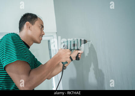 portrait of young man used a drill on the wall in the office room Stock Photo