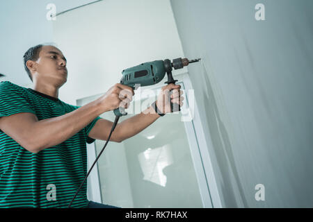 portrait of young worker use a drill make hole for a hangers on the wall behind door glass Stock Photo