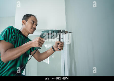 portrait of young man used a drill on the wall in the office room Stock Photo