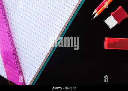 School and drawing supplies, on black background. Exercise book, pencils, eraser, sharpener and ruler. With copy space. Stock Photo