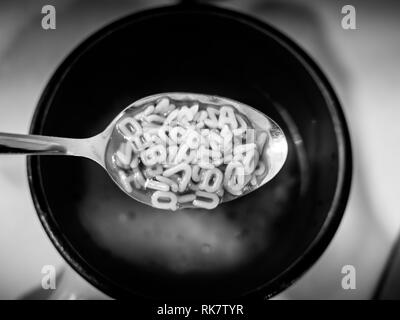 Image of black and white alphabet noodels soup with spoon Stock Photo