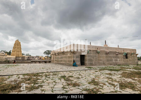 A woman in blue saree sits resting against amn old stone structure in Hampi, Karnataka with Virupakshara Temple in the backdrop. Stock Photo