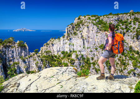 Happy hiker woman with backpack and photo camera enjoying the view from the high cliffs. Woman is standing on top of viewpoint near Cassis, Calanques  Stock Photo