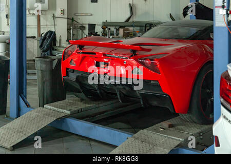 A sports car raised on a lift for repair and under it a detached engine ...