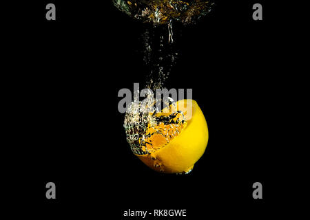 half a lemon falling in water on a black background Stock Photo