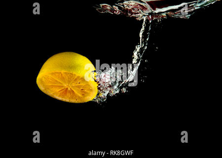 half a lemon falling into water on a black background Stock Photo