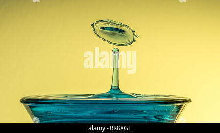 The moment two water droplets collide forming a crown. The liquid is coloured blue and the background is yellow. Water splash with copy space Stock Photo