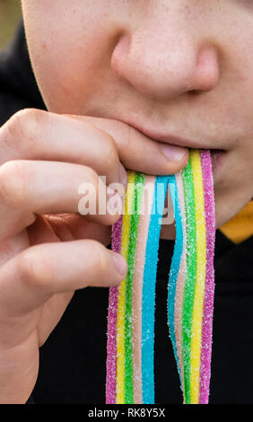 Child eat jelly colorful candy with sugar. Close-up child face and candy. Rainbow colours. Stock Photo