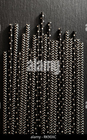 Black contrast drinking straws. Background of patterned straws on dark stone table. Arranged straws next to each other. Concept for Summer time and dr Stock Photo