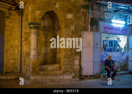 Man smoking a water pipe in front of his shop near a mosque in Acre, Israel Stock Photo