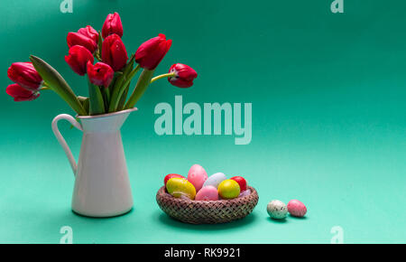 Easter eggs, pastel colors painted and tulips in a vase, green background, front view, copy space Stock Photo
