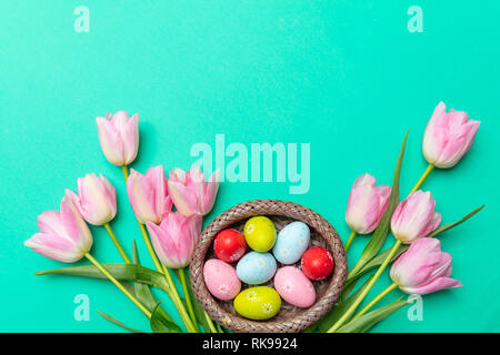 Easter eggs, pastel colors painted and pink tulips bouquet, green background, top view, copy space Stock Photo