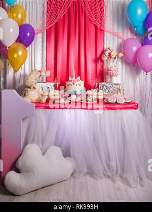 First baby girl birthday party concept. Candy bar with sweet unicorn cakes and decor items in bright pink colors. Stock Photo