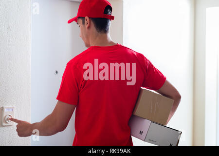 Courier man carrying cardboard boxes ringing the doorbell Stock Photo