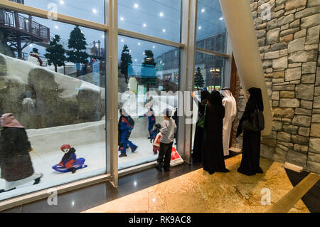 Visitors and families watching through large glass windows of skiers skiing on real snow at the Ski Dubai inside the Mall of the Emirates shopping mal Stock Photo