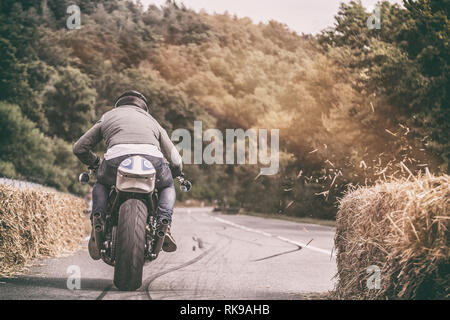 Motorcycle rider accelerating his bike on a straight forest road with pieces of hay blowing off a hay bale Stock Photo