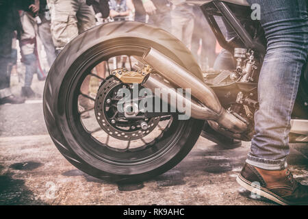 Motorcycle burnout and rear wheel spinning at the start of a drag race surrounded by bystanders Stock Photo