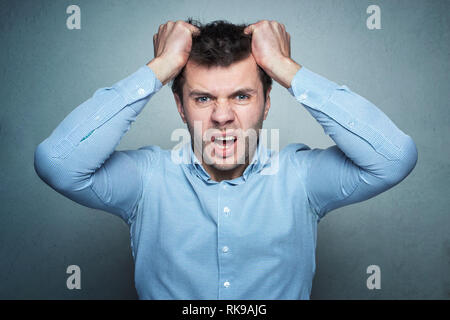 Portrait of frustrated young businessman pulling his hair on gray wall background Stock Photo
