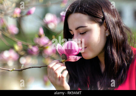 Beautiful girl smelling the flowers. Blossoming magnolia in the park garden. Stock Photo