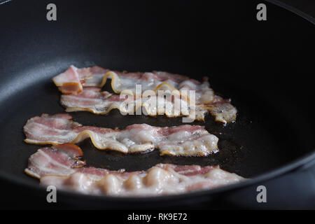Bacon slices being fried in frying pan. Stock Photo