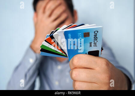 Confused man looking at many credit cards uncertain which one to choose on blue background. young man is holding a stop of credit and debit cards in a Stock Photo