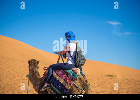 Tourist rides a camel through the sand dunes in the Sahara desert Stock Photo