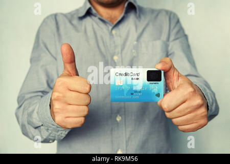 Cropped shot of young man in shirt holding credit card with biometric technology and showing thumb up. Man is glad to use bank card of new type. Advan Stock Photo