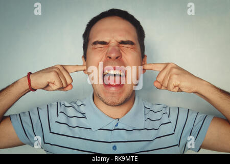 Studio shot of bothered and annoyed redhead caucasian man feeling discomfort hearing loud noise or serene, covering ears with index fingers like earpl Stock Photo