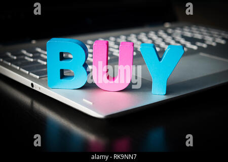 Buy word on laptop bottom at black background. Wooden colorful letters B, U, Y set on opened notebook. Concept of buying things in internet. Online sh Stock Photo