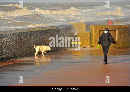 Waves breaking over seawall on Blackpool seafront on to women walking a dog Stock Photo