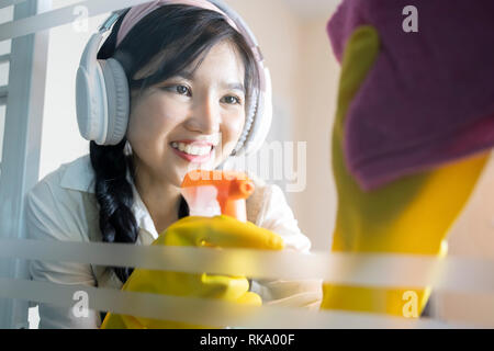 Asian woman hand with glove holding bottle of spray and using sponge to make window clean. Focus in happy face  - Image Stock Photo