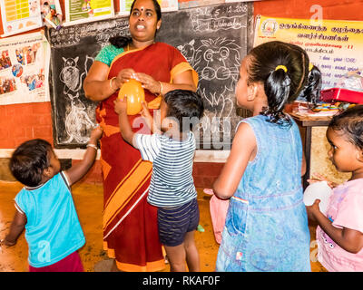 PUDUCHERY, INDIA - DECEMBER Circa, 2018. Poor preschool teacher and her group of kids boys girls having some fun at school with just a few wood toys g Stock Photo