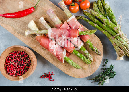 Fresh organic asparagus wrapped in Prosciutto ham on a cutting board. Stock Photo