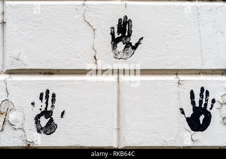 3 three black palm imprints on white large bricks with white peeling paint - high quality texture / background Stock Photo
