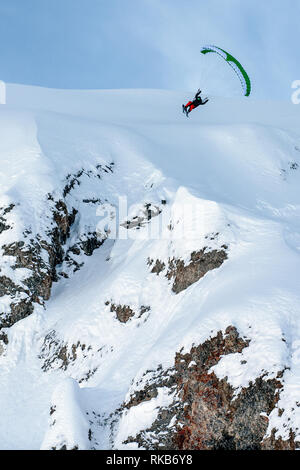 Speed-flying in the French alpine resort of Courchevel. A man flies using a speed-flying wing on skis off a cliff on snow. Stock Photo