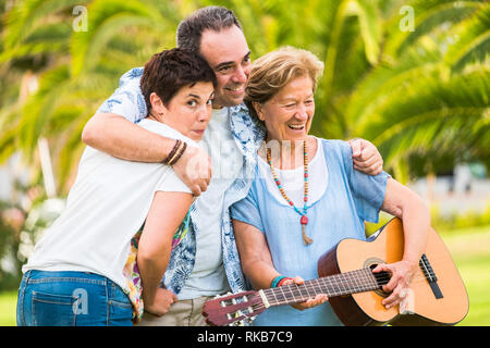 Different mixed ages generations together having fun in familyh portrait leisure activity - old woman play a guitar and laugh a lot - green natural ba Stock Photo
