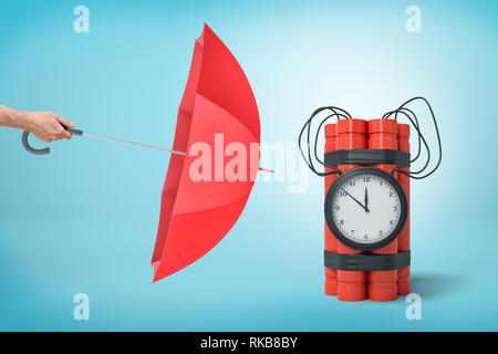 Male hand with red umbrella pointing to red dynamite time bomb on blue background Stock Photo