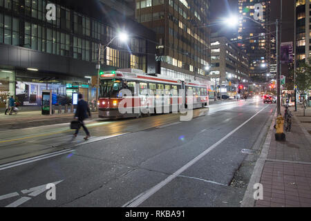 A banker crosses Bay Street as night falls on downtown Toronto. A streetcar waits on the road. Stock Photo