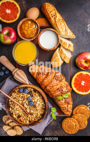 Healthy balanced breakfast on a dark background. Muesli, milk, juice, croissants top view. Stock Photo