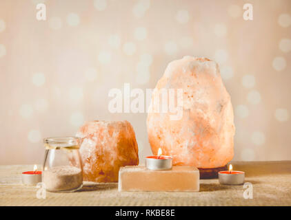 Himalayan Salt Soap bar, pink rock salt lamp turned on and salt candle holder, with candle burning inside, jar with salt grains on light bokeh backgro Stock Photo