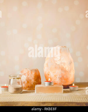 Himalayan Salt Soap bar, pink rock salt lamp turned on and salt candle holder, with candle burning inside, jar with salt grains on light bokeh backgro Stock Photo